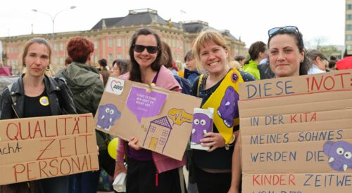 Der Landtag Brandenburg im Hintergrund. 4 Frauen mit Plakaten auf einer Demonstration. Die Frauen halten ihre Plakate in die Kamera und lächeln.